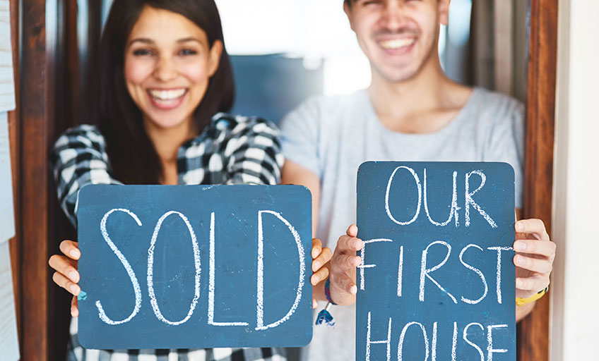 A couple holding a sign for their first house