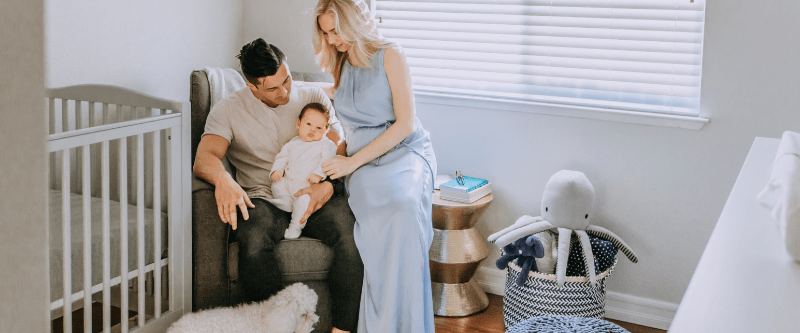 Mom, dad, newborn baby and puppy snuggling in baby's nursery. 